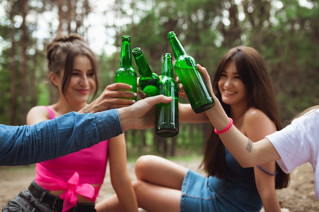 Glück. Gruppe von Freunden, die beim Picknick im Sommerwald Bierflaschen klirren.