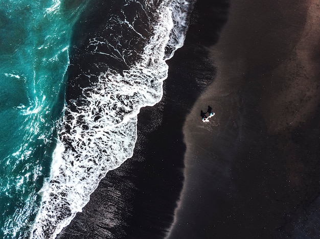 Glück-Paare, die auf schwarzem Sandstrand mit weißer Welle bei Bali, Indonesien genießen