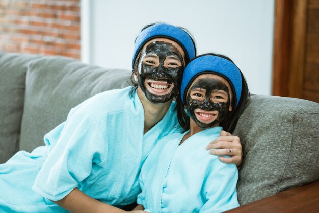 Glück von Mutter und Kind, wenn sie zusammen Gesichtsmasken aus Ton verwenden, während sie auf dem Sofa sitzen
