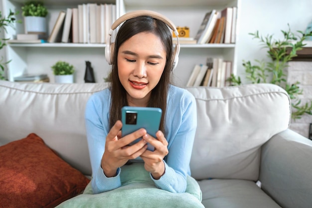 Foto glücklich entspannte junge frau sitzt auf einem sofa mit einem handy und hört musik über eine app und kopfhörer