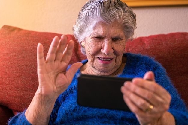 Glücklich lächelnde alte Frau fiel mit der Hand zur Begrüßung, während sie ein Smartphone benutzte