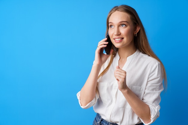 Glücklich lächelnde junge Frau am Telefon vor blauem Hintergrund the