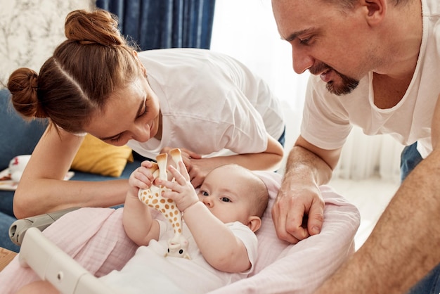 Glücklich lächelnde Mama und Papa beugten sich über ihr Baby, das in der Wiege lag und ein Giraffenspielzeug in der Hand hielt