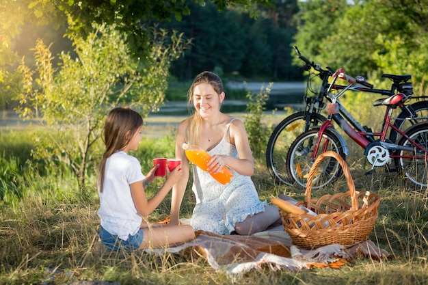 Glücklich lächelnde Mutter und Tochter trinken Orangensaft beim Picknick juice