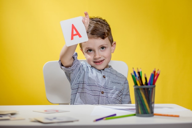 Glücklich lächelnder kleiner Vorschuljunge zeigt Briefe zu Hause, die am Morgen vor Schulbeginn Hausaufgaben machen