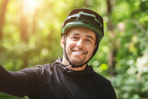 Glücklich lächelnder Radfahrer, der ein Selfie im grünen Wald macht