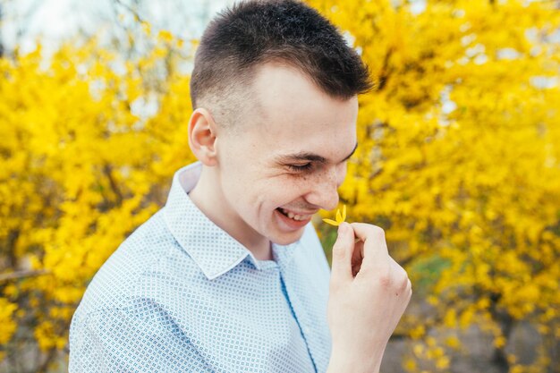 Glücklich lächelnder romantischer junger Mann mit gelben Frühlingsblumen im Garten