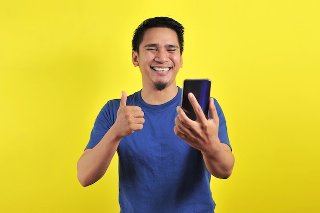Glücklich über den jungen, gut aussehenden asiatischen Mann, der mit dem Smartphone auf gelbem Hintergrund lächelt