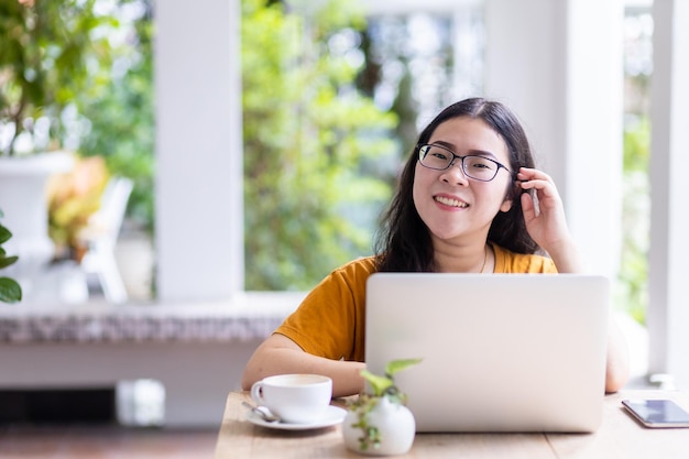 Glücklich von asiatischen freiberuflichen geschäftsfrauen, die lässig mit laptop-computer mit kaffeetasse und smartphone im café arbeiten, mögen das hintergrundkommunikationskonzept