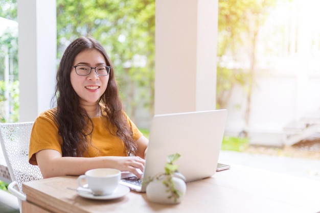 Glücklich von asiatischen freiberuflichen Geschäftsleuten, die beiläufig mit Laptop-Computer mit Kaffeetasse und Smartphone im Café arbeiten, wie der Hintergrund, Kommunikationskonzept