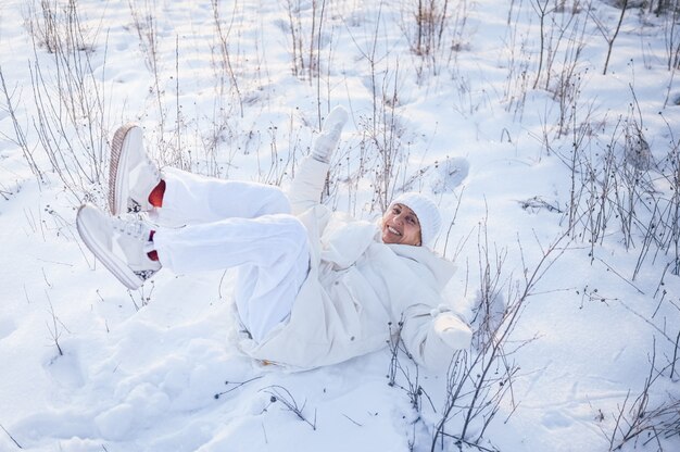 Glückliche ältere ältere reife Frau in der weißen warmen Oberbekleidung, die mit Schnee im sonnigen Winter draußen spielt