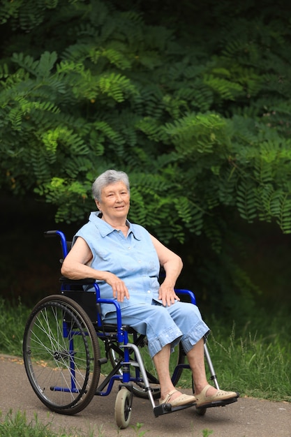 Glückliche ältere behinderte Frau, die im Rollstuhl draußen sitzt