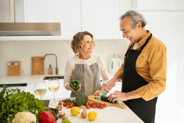 Glückliche ältere Ehepartner, die zusammen kochen und Frau und Mann sprechen, die Gemüsesalatküche zubereiten