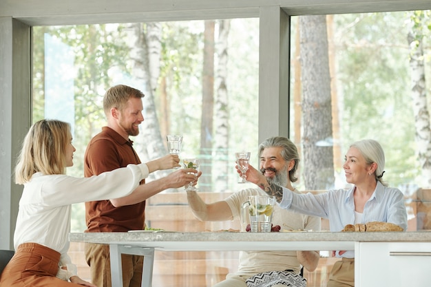 Glückliche ältere Eltern und ältere Kinder, die Gläser der Limonade beim Trinken anheben, um sich beim Familienessen zu versammeln