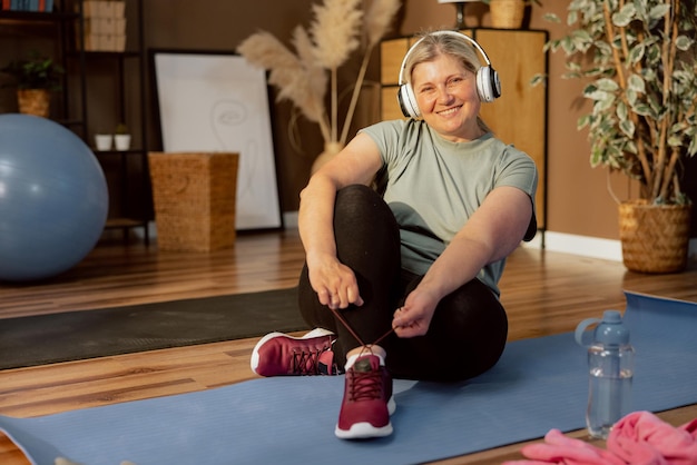 Glückliche ältere Frau, die auf einer Yogamatte sitzt, bindet Schnürsenkel, die während der Trainingsübungen ruhen