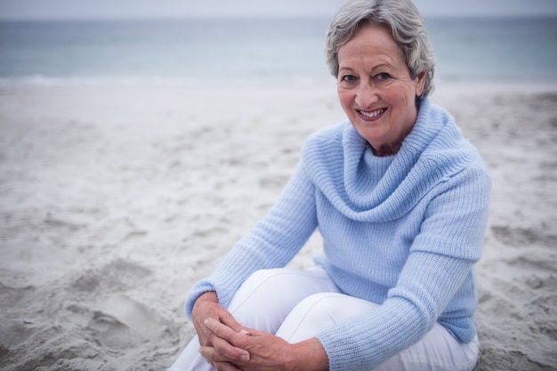 Glückliche ältere Frau, die auf Strand sitzt