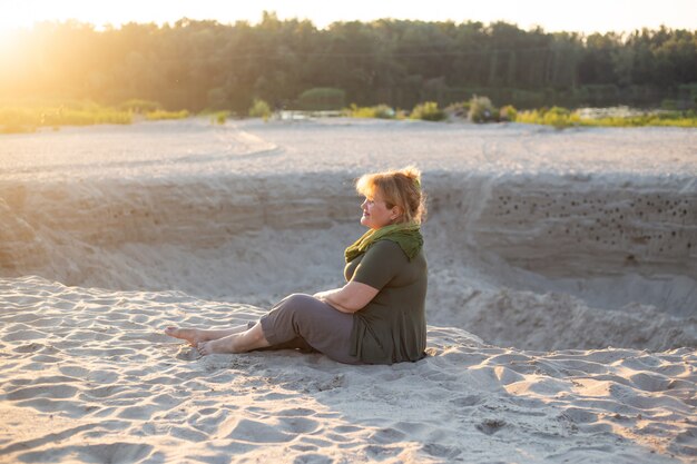 Glückliche ältere Frau, die draußen auf einem Sand draußen im Sommer sitzt