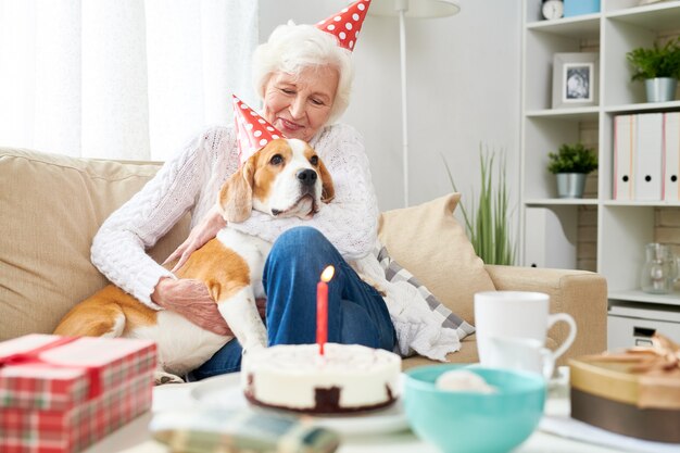 Glückliche ältere Frau, die Hund am Geburtstag umarmt