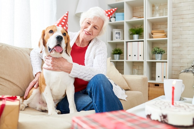 Glückliche ältere Frau, die Hund am Geburtstag umarmt