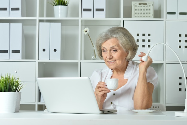 glückliche ältere Frau, die im Büro am Laptop arbeitet