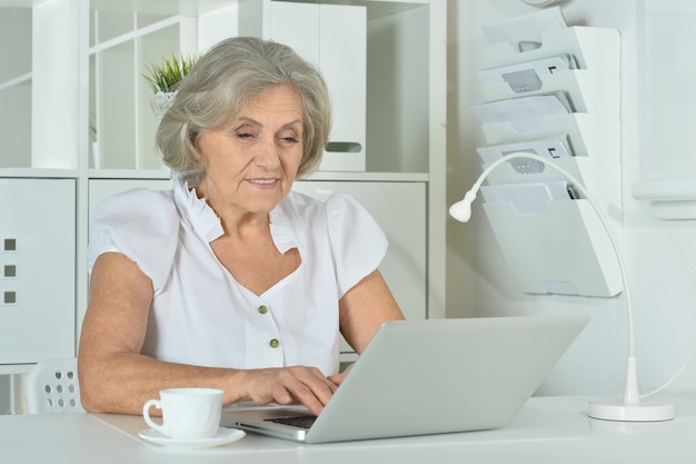 Glückliche ältere Frau, die im Büro am Laptop arbeitet