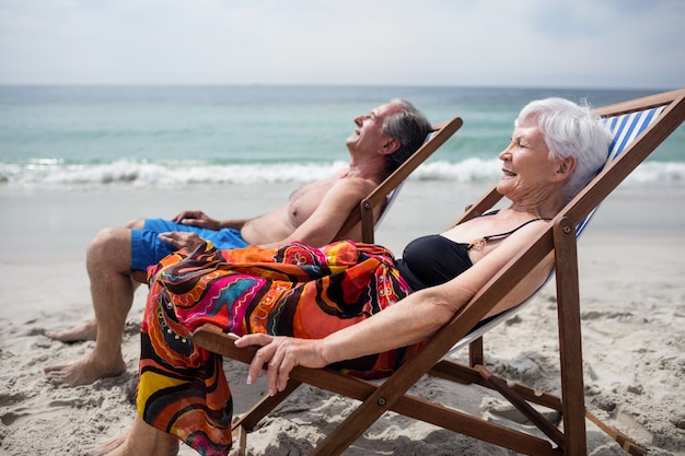 Glückliche ältere Paare, die auf Deckchairs am Strand sich entspannen