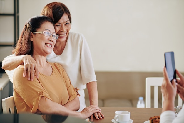 Glückliche ältere vietnamesische Freundinnen, die sich umarmen und für ein Foto auf dem Smartphone posieren