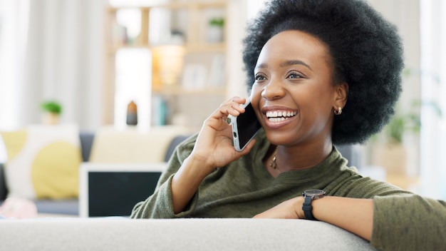 Glückliche Afrikanerin telefoniert, während sie sich zu Hause auf ihrem gemütlichen Sofa entspannt. Fröhliche schwarze Frau mit Afro-Lachen, während sie ein angenehmes und lustiges Gespräch mit einer Freundin auf ihrem Handy führt