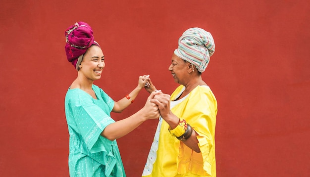Glückliche afrikanische Mutter und Tochter tanzen zusammen, während sie traditionelle Kleidung tragen. Mutterschaftsmusik, ethnische Kulturen und Familienkonzept. Fokus auf Gesichter