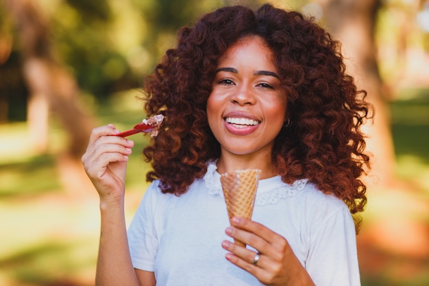 Glückliche Afro-Frau, die Eis im Park isst.