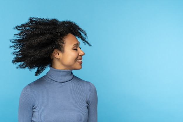 Glückliche Afro-Frau lächelt, hat gute Laune und tanzt mit ihrem schwarzen lockigen Haar fliegend