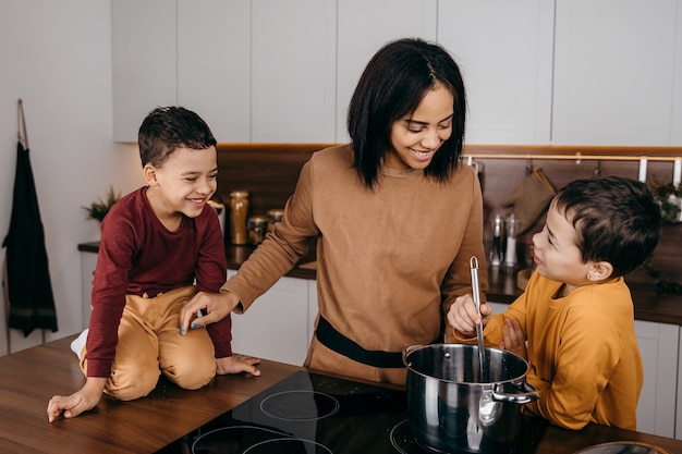 Glückliche afroamerikanische Familienmutter und zwei Söhne, die Spaß beim Kochen des Mittagessens in der Küche haben