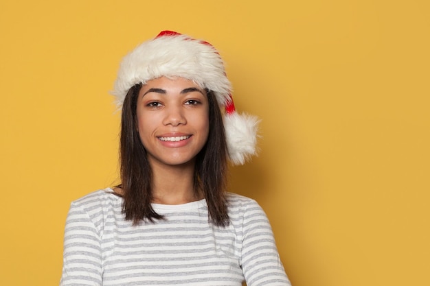 Glückliche afroamerikanische Frau mit Weihnachtsmannshut lächelt auf gelbem Hintergrund