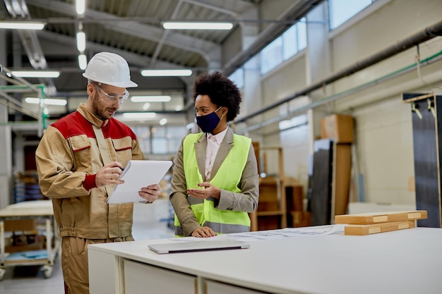 Glückliche afroamerikanische Geschäftsfrau, die mit einem Arbeiter in einer Holzbearbeitungsfabrik spricht