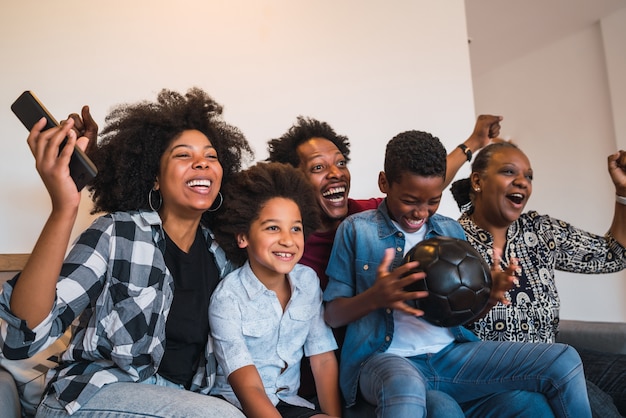 Glückliche afroamerikanische Mehrgenerationenfamilie, die Fußballspiel im Fernsehen im Wohnzimmer zu Hause sieht