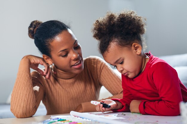 Glückliche afroamerikanische Mutter, die ihrer Tochter beim Färben hilft