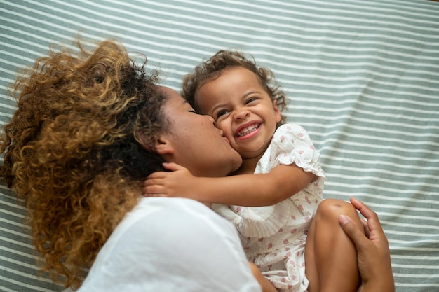 Glückliche afroamerikanische Mutter, die zu Hause mit ihrem Mädchen im Schlafzimmer spielt