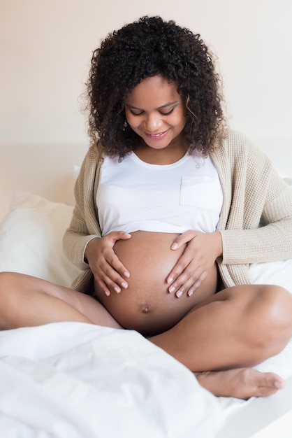 Glückliche Afrofrau, die ihren schwangeren Bauch zeigt