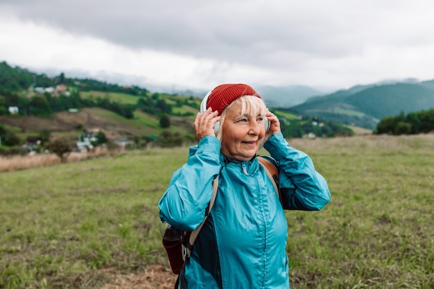 Glückliche aktive ältere Touristin, die Musik hört und die Landschaft bewundert