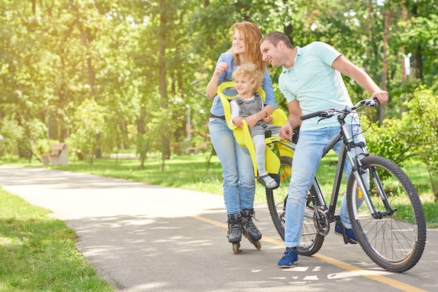 Glückliche aktive Familie, die im Sommer Inlineskaten und Radfahren im Park genießt.