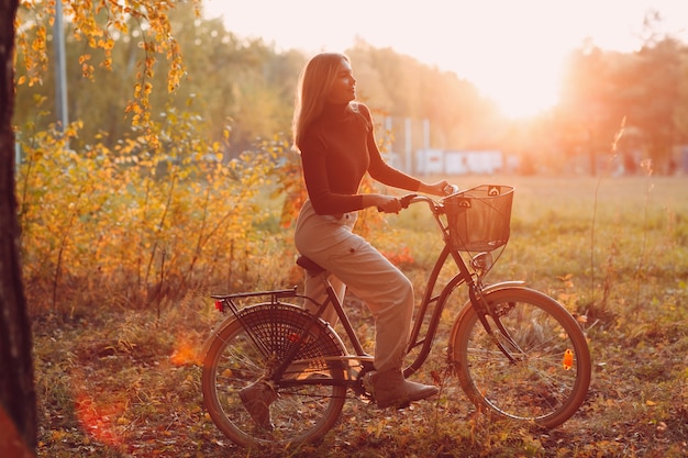 Glückliche aktive junge Frau, die bei Sonnenuntergang Vintage-Fahrrad im Herbstpark reitet.