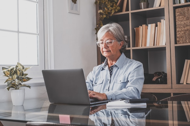 Glückliche alte kaukasische Geschäftsfrau, die lächelt, online arbeitet, Webinar-Podcast auf dem Laptop sieht und Bildungskurskonferenzen anruft, machen Notizen am Schreibtisch sitzen, E-Learning-Konzept