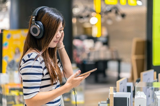 Glückliche Asiatin, die Technologie Kopfhörer oder Kopfhörer hört und prüft