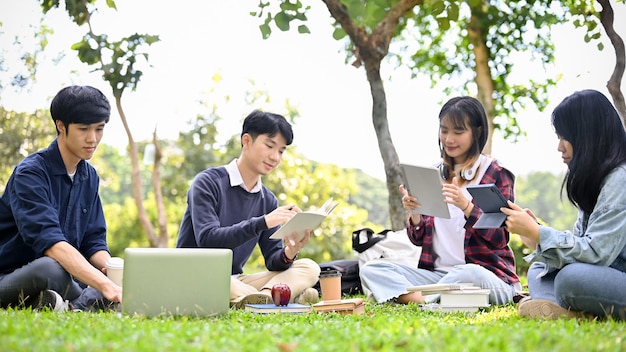 Glückliche asiatische College-Studenten arbeiten gemeinsam an ihrem Projekt, während sie sich im Park entspannen