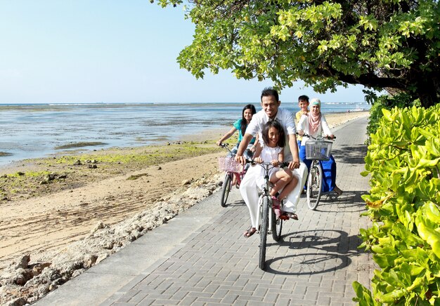 Glückliche asiatische Familie, die Fahrrad am schönen Morgen am Strand reitet