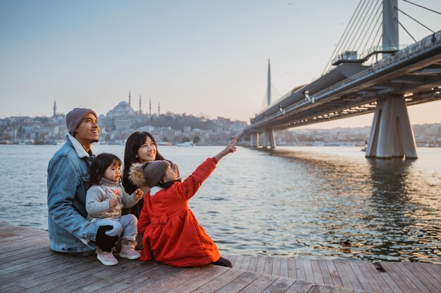 Glückliche asiatische Familie sitzt am Ufer des Bosporus und blickt auf den wunderschönen Sonnenuntergang in Istanbul, Türkei