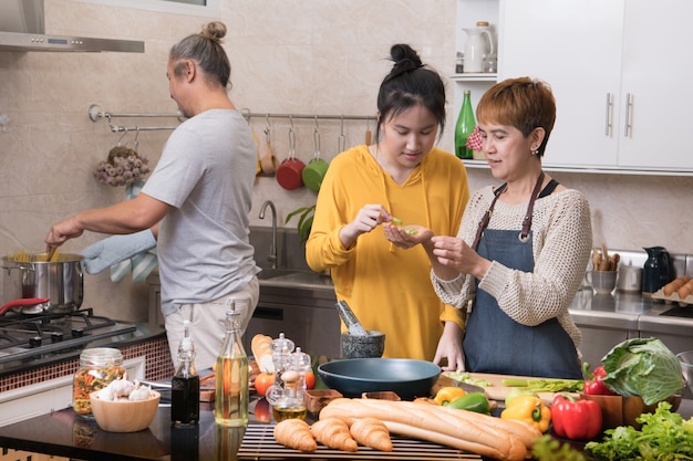 Glückliche asiatische Familie von Mutter, Vater und Tochter, die in der Küche kochen, die zusammen gesundes Essen macht, das Spaß fühlt