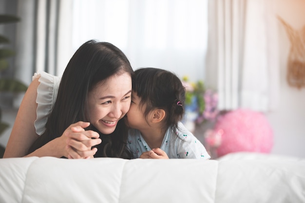 Glückliche asiatische Familienmutter mit der Tochter, die auf Bett mit Lächelngesicht spielt