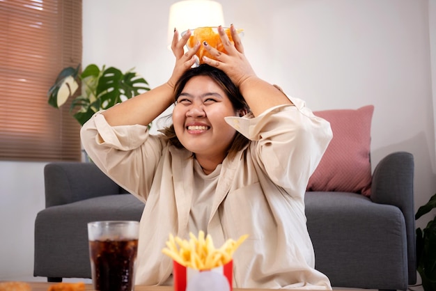 Glückliche asiatische fette Frau isst gerne leckere Pommes Frites und Kartoffelchips im Wohnzimmer