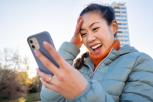 Glückliche asiatische Frau, die das Smartphone im Freien nutzt. Echtes Menschen- und Technologiekonzept